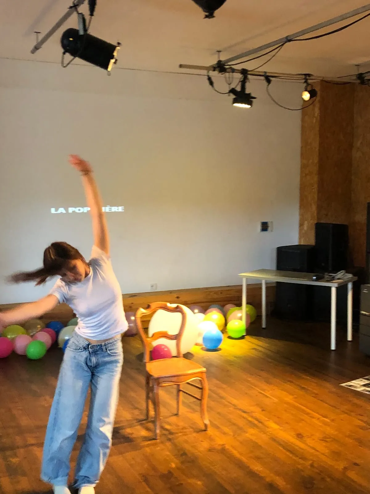 Une danseuse en plein saut sur la scène, au milieu des ballons, devant un mur où le nom de la POPinière est projeté