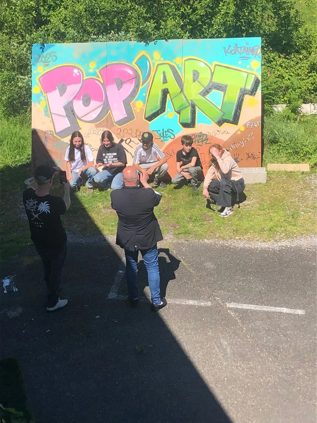Six jeunes posant devant une fresque graffiti peinte à la main, deux adultes les photographiant