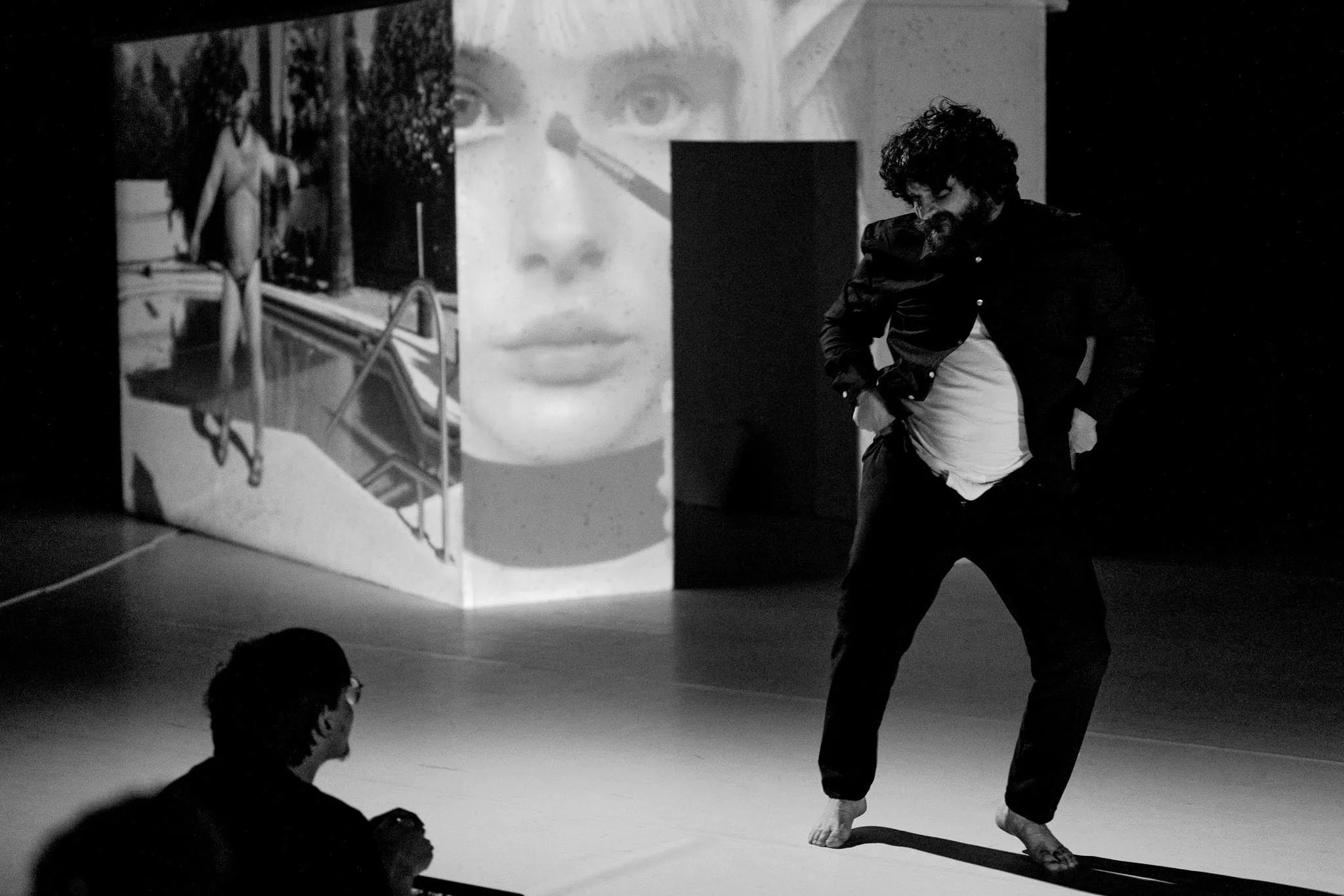 Spectacle au Kontainer : une interprète danseuse pieds nus devant une projection vidéo, un spectateur au premier plan
